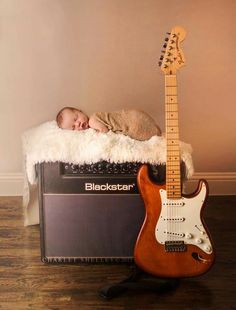 a baby sleeping next to an electric guitar and amp with a blanket on top of it