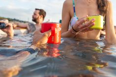 two people are sitting in the water and one person is holding a cup with something on it