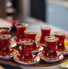 there are many cups and saucers on the tray with red liquid in them as well