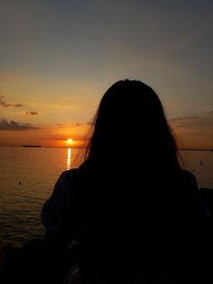 a woman is looking out at the sunset