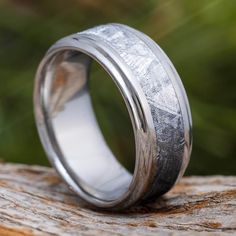 a wedding ring with silver inlays sitting on top of a piece of wood