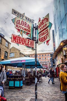 people are walking down the street in front of some shops and signs that read west yard, global kitchen, north market, middle market