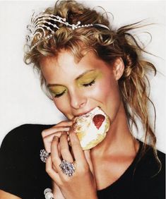 a woman wearing a tiara eating a donut with green eyeshadow and gold makeup