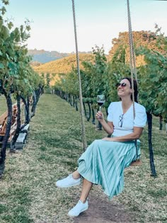 a woman sitting on a swing in a vineyard