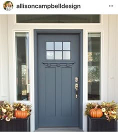 a gray front door with two planters and pumpkins