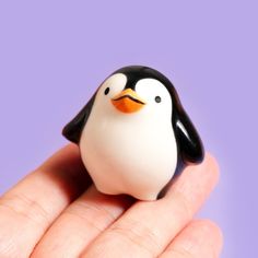 a small toy penguin sitting on top of someone's hand in front of a purple background