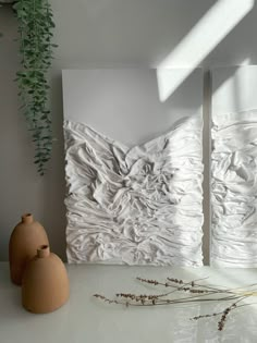 two vases sitting next to each other on a white table with paintings behind them