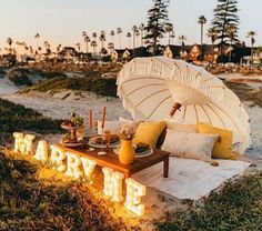 an umbrella is set up on the beach for a picnic with food and drinks in front of it