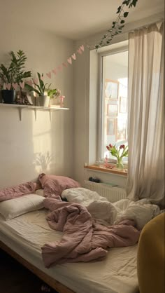 an unmade bed in front of a window with pink sheets and pillows on it