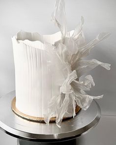 a white frosted cake on a silver platter with plastic wrap around the edges