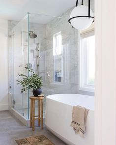 a white bath tub sitting next to a window in a bathroom under a light fixture