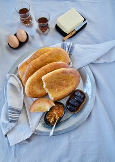 a plate with bread, butter and jelly on it next to two glasses of juice