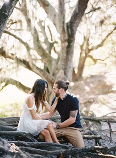 a man and woman sitting on top of a tree trunk