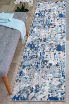 an area rug with blue and white paint splattered on the floor in front of a couch