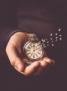 a person holding an alarm clock in their hands with butterflies coming out of the top