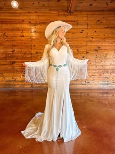 a woman in a white dress and cowboy hat posing for a photo with her arms outstretched