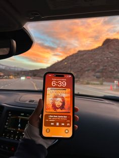 someone is holding up their cell phone while driving in the car with mountains in the background