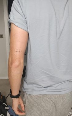 the back of a man's arm with a small tattoo on his left arm