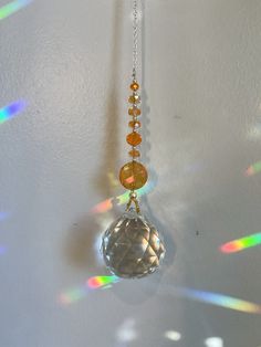 the sun shines brightly on a glass ornament hanging from a chain in front of a white wall