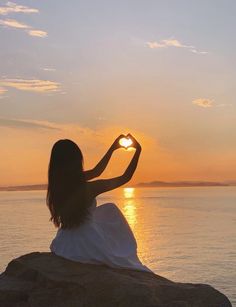 a woman sitting on top of a rock near the ocean holding a heart shaped object