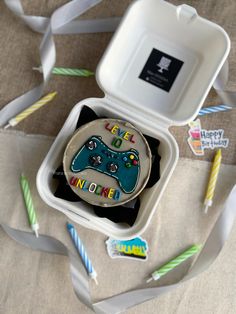 a birthday cake with a video game controller on it in a box surrounded by candles and streamers