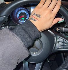 a woman's hand on the steering wheel of a car with her wrist tattoo