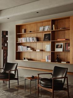 two chairs and a table in front of a bookshelf with shelves on the wall