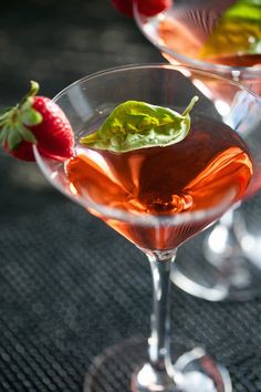 two martinis with strawberries and basil garnish sit on a black table