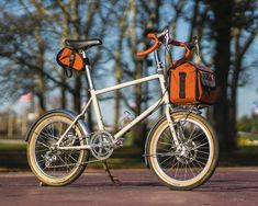 a white bicycle with an orange bag on the front and back tire, parked in a parking lot