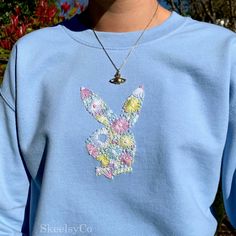 a person wearing a blue sweatshirt with a floral rabbit on it's chest and necklace