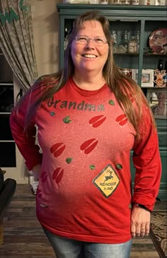 a woman standing in front of a book shelf wearing a red shirt that says grandma