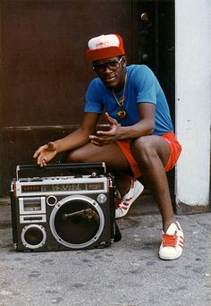 a man sitting on the ground next to an old radio and wearing a red hat