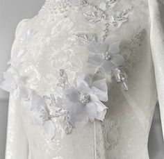 a white dress with flowers and pearls on the neckline is shown in close up