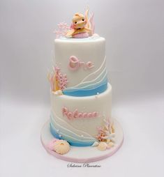 a three tiered cake with an ocean theme on the top and bottom layer is decorated with shells, seashells, and a teddy bear