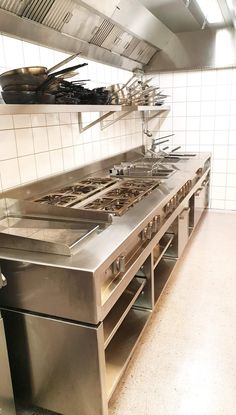 an industrial kitchen with stainless steel appliances and white tiled walls, along with black pots and pans on the stovetop