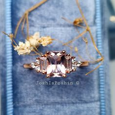 an engagement ring with three stones and flowers in the background on top of a blue velvet box