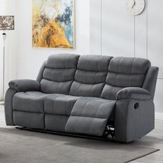 a grey reclining couch in a living room with a clock on the wall behind it