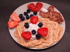 pancakes with strawberries, blueberries and bacon are on a plate next to meat