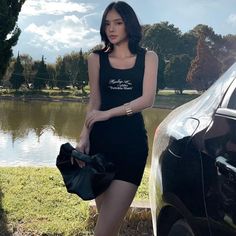 a woman standing next to a black car in front of a body of water and trees