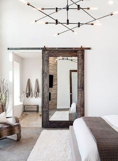 a bedroom with a bed, chair and large mirror in the room that has lights hanging from the ceiling