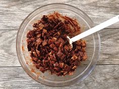 a glass bowl filled with chopped up food on top of a wooden table next to a white spoon