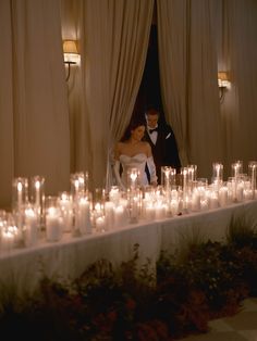 a bride and groom standing in front of a long table with lit candles on it