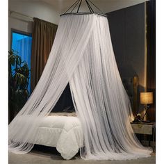 a canopy bed with white netting on it in a bedroom next to a lamp and window