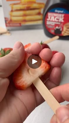 a person holding a toothpick with food on it and strawberries in the background