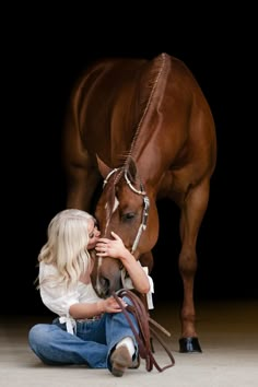 a woman kneeling down next to a brown horse with its head on it's hind legs