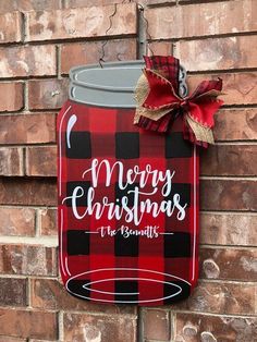 a red and black plaid christmas mason jar sign hanging on a brick wall with a bow