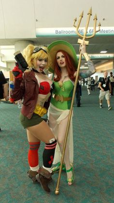 two women dressed in costumes pose for the camera at an airport terminal, one holding a staff