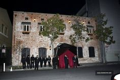 a group of people standing in front of a brick building at night with lights on