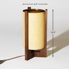 a wooden table lamp with a paper shade on the bottom and an electric cord attached to it