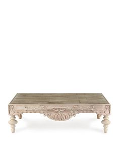 a white coffee table with carvings on the top and bottom, against a white background